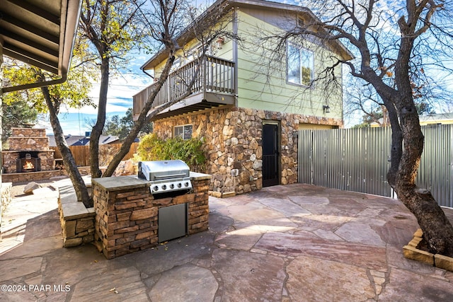 view of patio / terrace with an outdoor stone fireplace, a grill, a balcony, and exterior kitchen