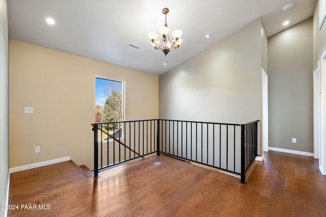 spare room featuring lofted ceiling, wood-type flooring, and an inviting chandelier