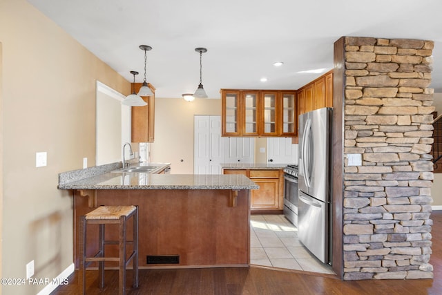 kitchen with sink, stainless steel appliances, light hardwood / wood-style flooring, kitchen peninsula, and pendant lighting