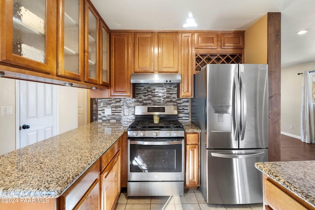 kitchen with light tile patterned floors, light stone countertops, appliances with stainless steel finishes, and tasteful backsplash