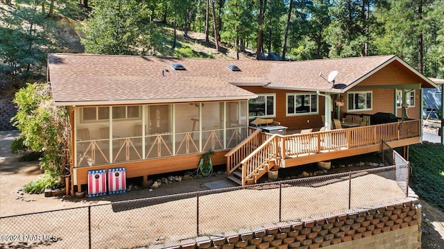 back of house with a wooden deck, fence, roof with shingles, and a sunroom