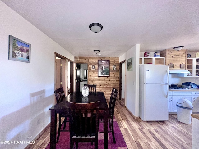 dining area featuring a textured ceiling, light wood-type flooring, and wooden walls