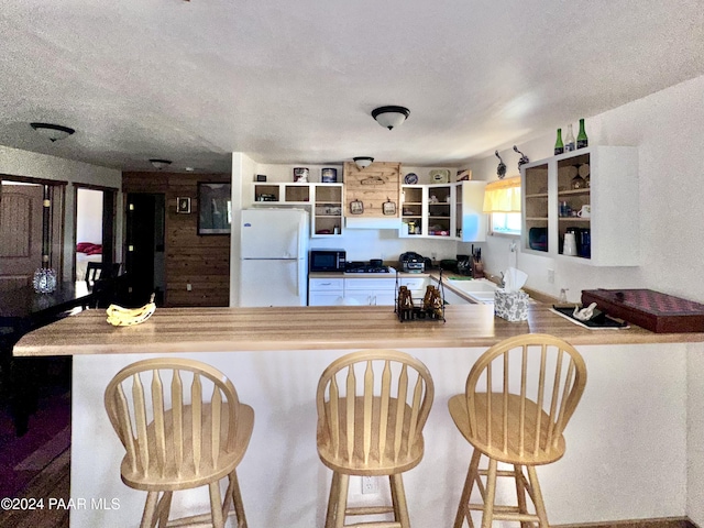 kitchen featuring a kitchen breakfast bar, kitchen peninsula, white fridge, and a textured ceiling