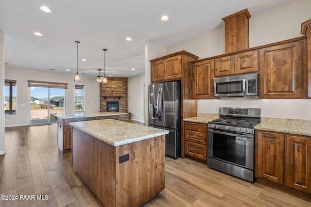 kitchen with hanging light fixtures, stainless steel appliances, light stone counters, light hardwood / wood-style flooring, and a kitchen island