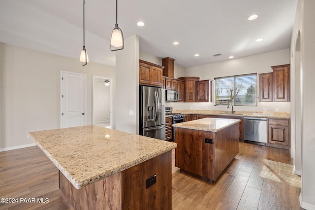 kitchen featuring light stone countertops, pendant lighting, wood-type flooring, a kitchen island, and appliances with stainless steel finishes