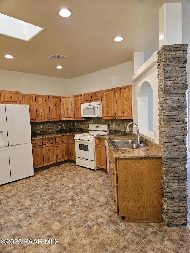 kitchen featuring sink, white appliances, a skylight, and backsplash