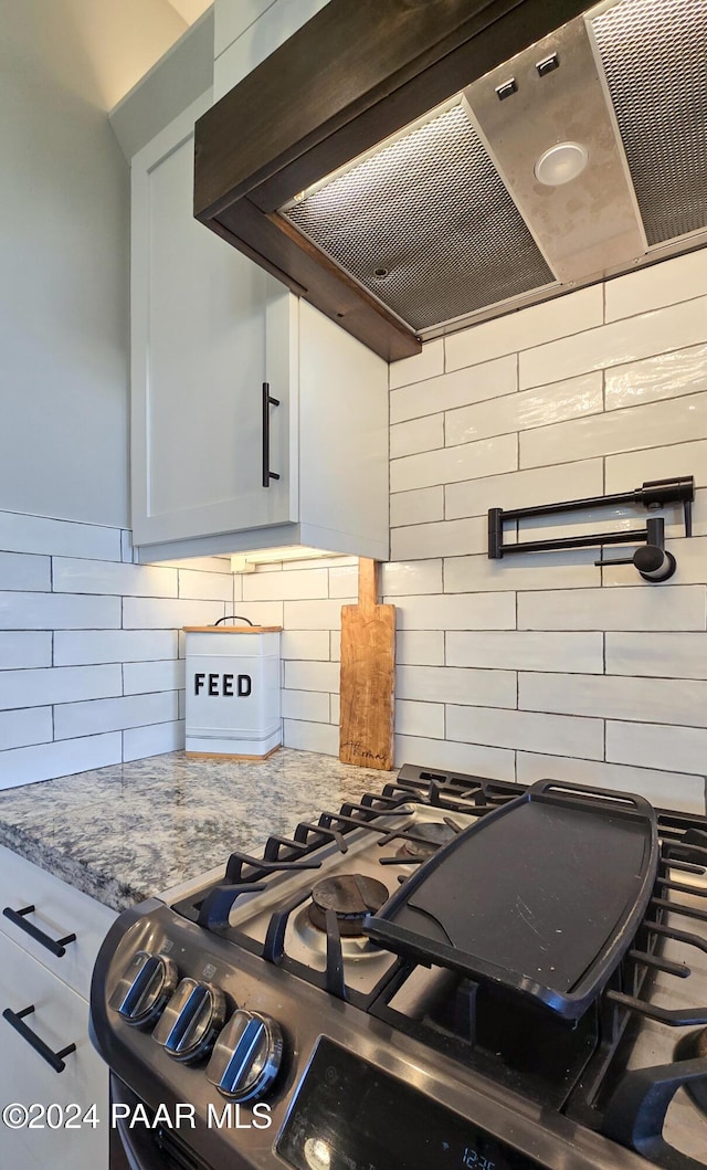 kitchen featuring light stone countertops, white cabinetry, range with gas stovetop, decorative backsplash, and wall chimney exhaust hood