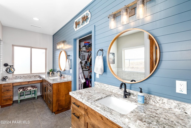 full bath featuring a wealth of natural light, two vanities, a walk in closet, and a sink