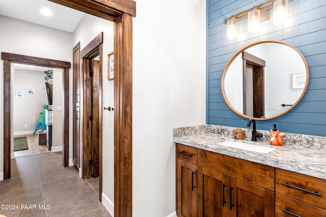 bathroom with wood walls, vanity, baseboards, and tile patterned floors