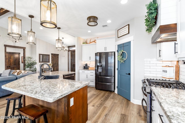 kitchen featuring a center island with sink, stainless steel appliances, hanging light fixtures, open floor plan, and white cabinets