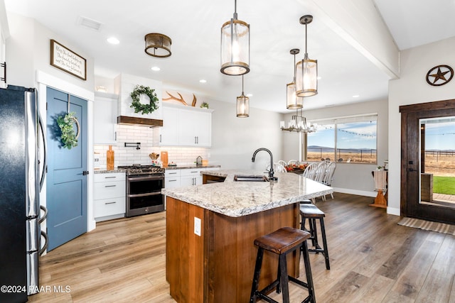 kitchen featuring a kitchen island with sink, a sink, white cabinets, appliances with stainless steel finishes, and decorative light fixtures