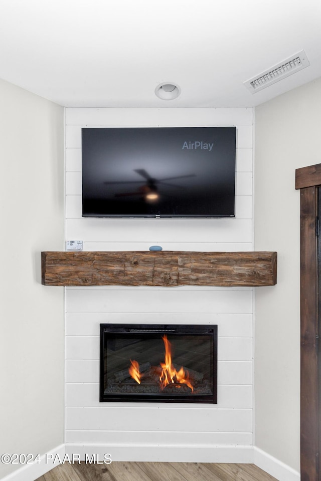 room details with a large fireplace, visible vents, baseboards, and wood finished floors