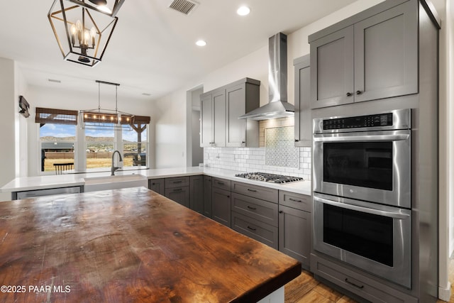 9550 N Manger Rd, Prescott Valley, AZ 86314 - kitchen with appliances with stainless steel finishes, wall chimney range hood, gray cabinetry, a chandelier, and wood finished floors
