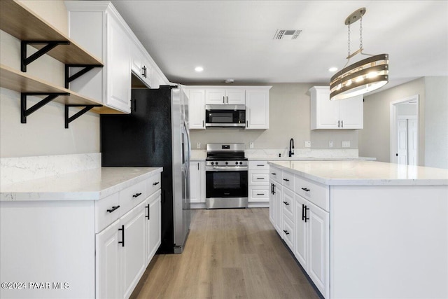 kitchen with sink, decorative light fixtures, white cabinetry, wood-type flooring, and stainless steel appliances