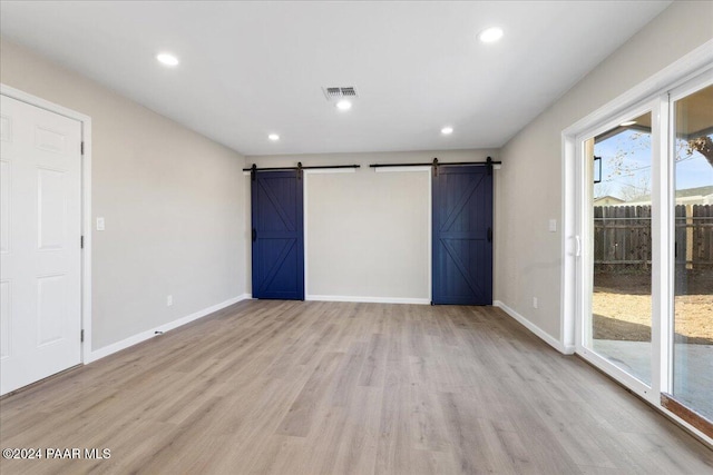 unfurnished bedroom featuring a barn door, light hardwood / wood-style flooring, and access to exterior