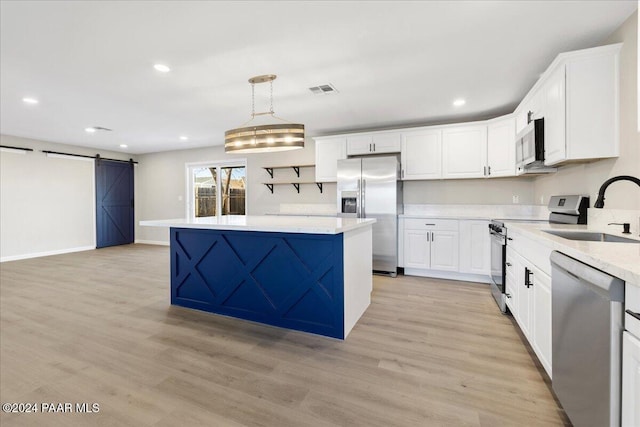 kitchen with sink, light hardwood / wood-style flooring, a barn door, appliances with stainless steel finishes, and decorative light fixtures