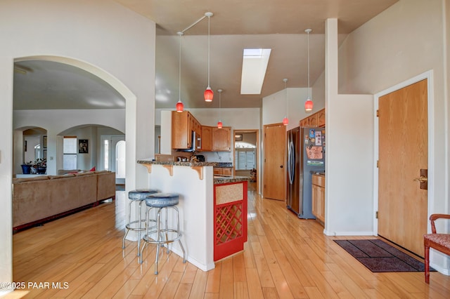 kitchen with appliances with stainless steel finishes, a kitchen breakfast bar, dark stone counters, light hardwood / wood-style floors, and kitchen peninsula