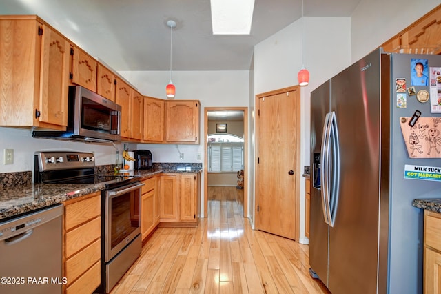 kitchen featuring appliances with stainless steel finishes, light wood-type flooring, and dark stone counters