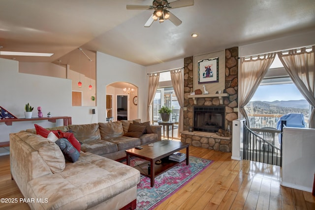 living room with a stone fireplace, vaulted ceiling, a mountain view, light hardwood / wood-style floors, and ceiling fan with notable chandelier