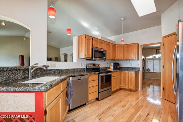 kitchen featuring sink, hanging light fixtures, light wood-type flooring, appliances with stainless steel finishes, and vaulted ceiling with skylight