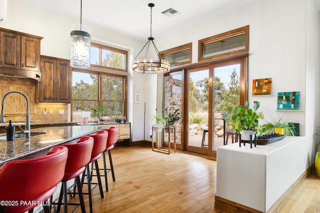 kitchen featuring sink, decorative light fixtures, light wood-type flooring, a kitchen breakfast bar, and dark stone counters