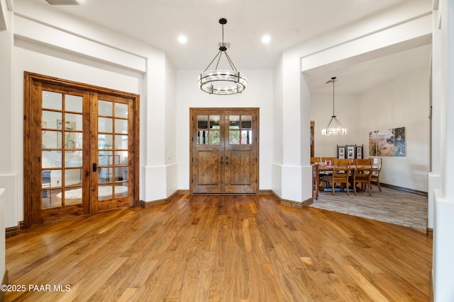 foyer entrance with wood-type flooring, a notable chandelier, and french doors