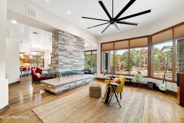 living room featuring ceiling fan, a multi sided fireplace, and light hardwood / wood-style floors