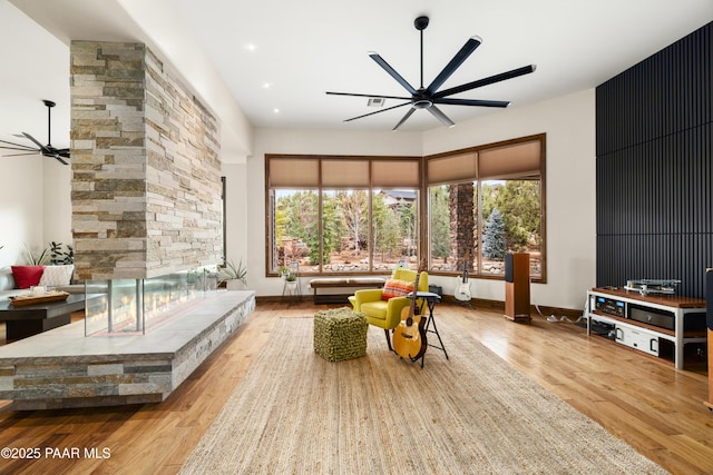 living room with a stone fireplace, ceiling fan, and light wood-type flooring