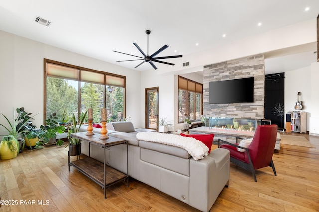 living room with a tile fireplace, ceiling fan, and light wood-type flooring