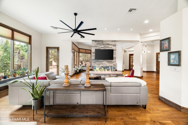 living room with ceiling fan with notable chandelier, a healthy amount of sunlight, a stone fireplace, and light hardwood / wood-style floors