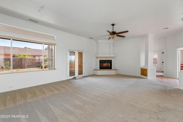 unfurnished living room with ceiling fan, a warm lit fireplace, visible vents, and light colored carpet