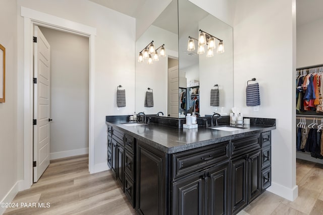 bathroom with a walk in closet, double vanity, a sink, and wood finished floors