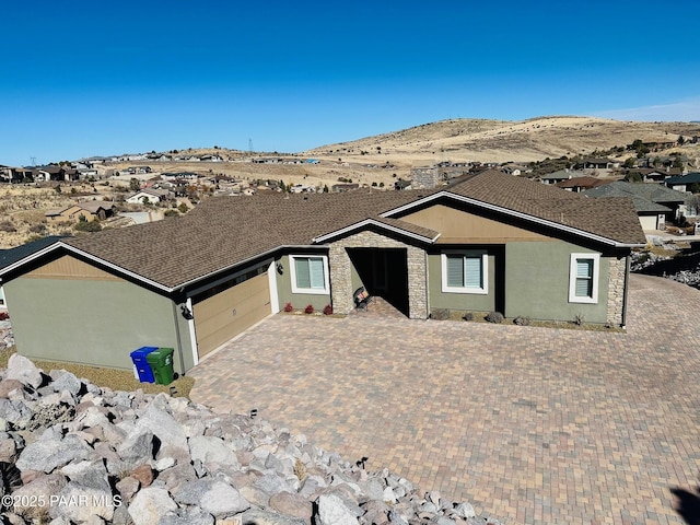 single story home with decorative driveway, stucco siding, an attached garage, a mountain view, and stone siding