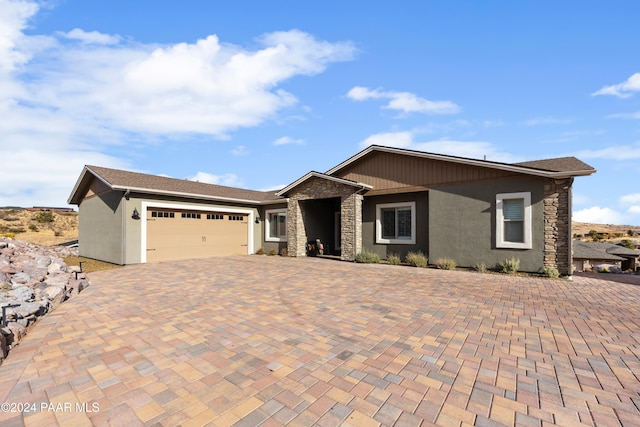 ranch-style house featuring a garage, stone siding, decorative driveway, and stucco siding