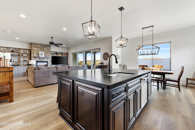 kitchen with light wood finished floors, dark countertops, a stone fireplace, a sink, and recessed lighting