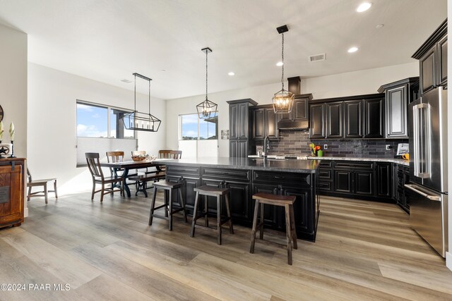 kitchen with visible vents, high end fridge, light wood-type flooring, backsplash, and a kitchen bar