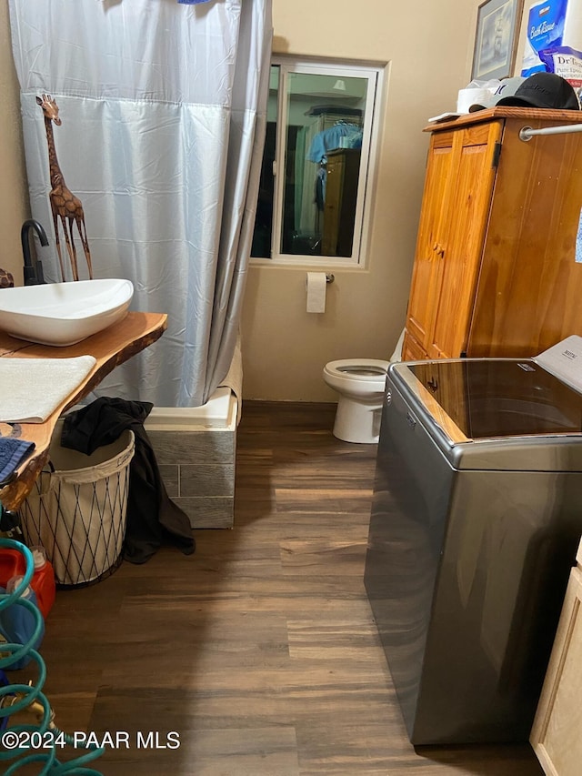 full bathroom with wood-type flooring, washer / dryer, sink, toilet, and shower / bathtub combination with curtain