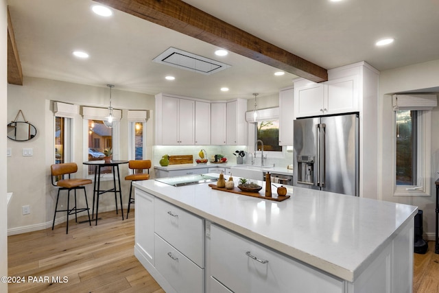 kitchen with beam ceiling, stainless steel appliances, white cabinetry, and light hardwood / wood-style flooring