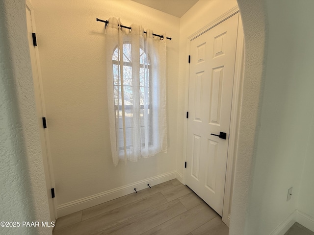 entryway featuring baseboards, light wood-style floors, and a textured wall