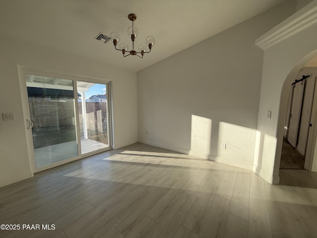 empty room with visible vents, a notable chandelier, wood finished floors, a barn door, and arched walkways