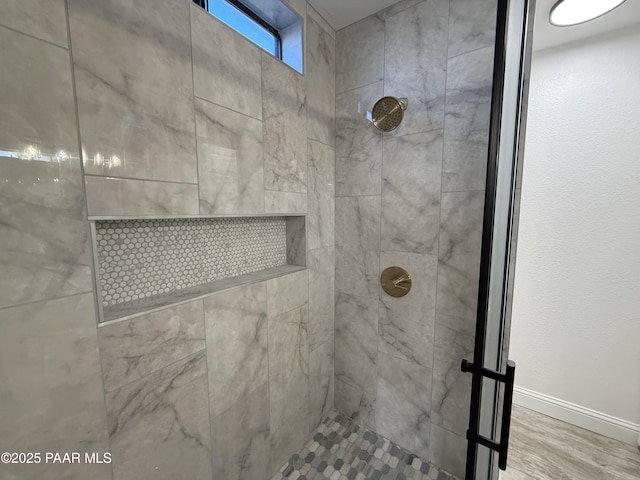 full bath with wood finished floors, baseboards, and a tile shower