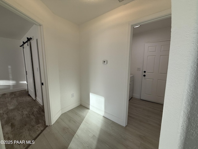 corridor featuring baseboards, light wood-style floors, and a barn door