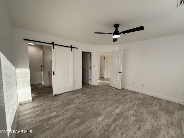 unfurnished bedroom with baseboards, a barn door, wood finished floors, a textured ceiling, and a ceiling fan