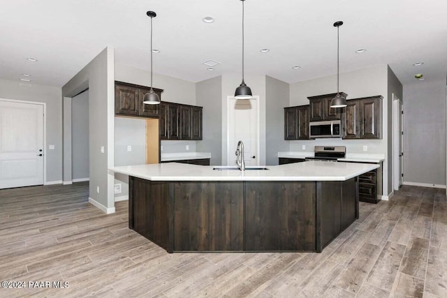 kitchen with light wood-type flooring, stainless steel appliances, sink, a large island with sink, and hanging light fixtures