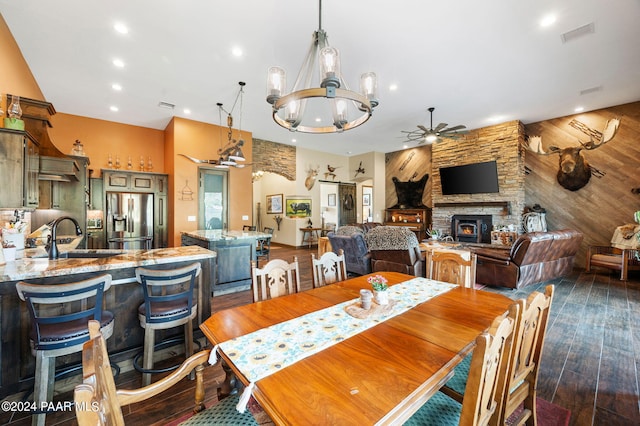 dining room featuring a stone fireplace, sink, ceiling fan with notable chandelier, and dark hardwood / wood-style flooring