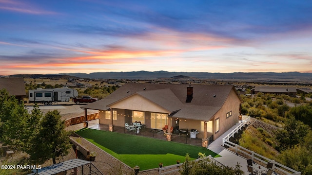 back house at dusk featuring a mountain view, a yard, and a patio