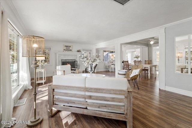 living room featuring ceiling fan, dark hardwood / wood-style flooring, crown molding, and a brick fireplace