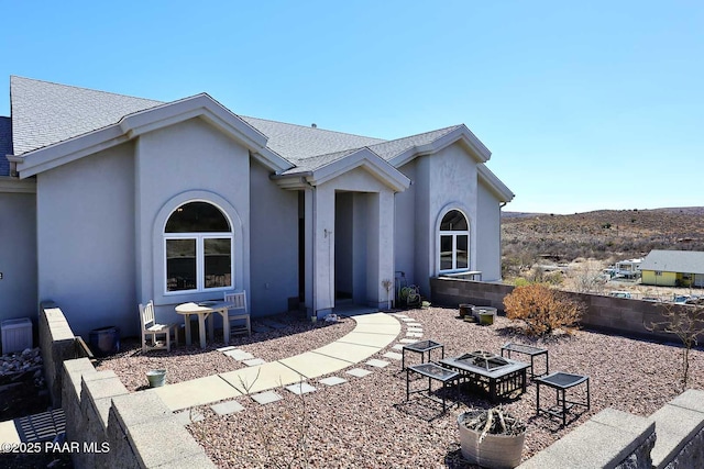 view of front of property featuring stucco siding, a patio, a fire pit, and roof with shingles