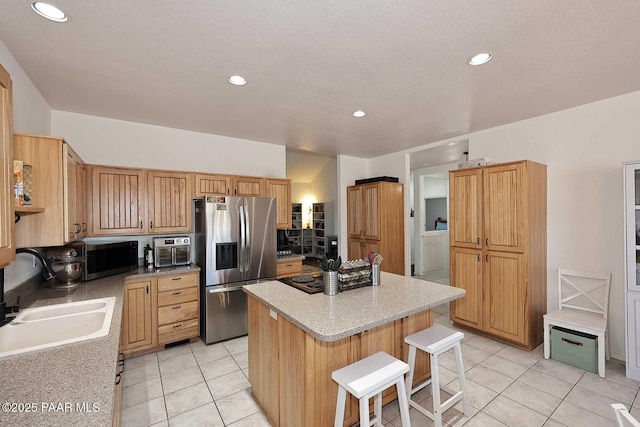 kitchen featuring light tile patterned floors, a sink, appliances with stainless steel finishes, a kitchen breakfast bar, and a center island