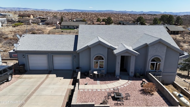 ranch-style home featuring stucco siding, driveway, a mountain view, an attached garage, and a shingled roof